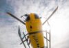 Yellow helicopter seen from below with spinning rotor against a bright sky