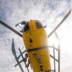 Yellow helicopter seen from below with spinning rotor against a bright sky