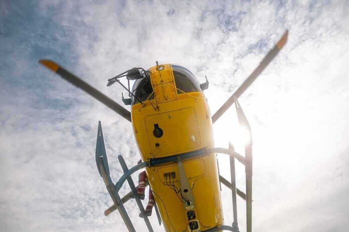 Yellow helicopter seen from below with spinning rotor against a bright sky