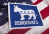 Wacky Dem Candidate Writes Song Hoping Senator Would Die Democrats donkey symbol on a blue sign over an American flag
