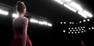 Model in a red dress walking on a runway under bright stage lights