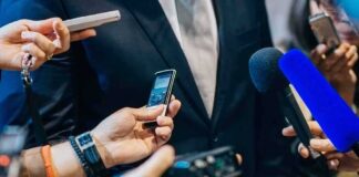 businessperson in suit surrounded by microphones and recorders