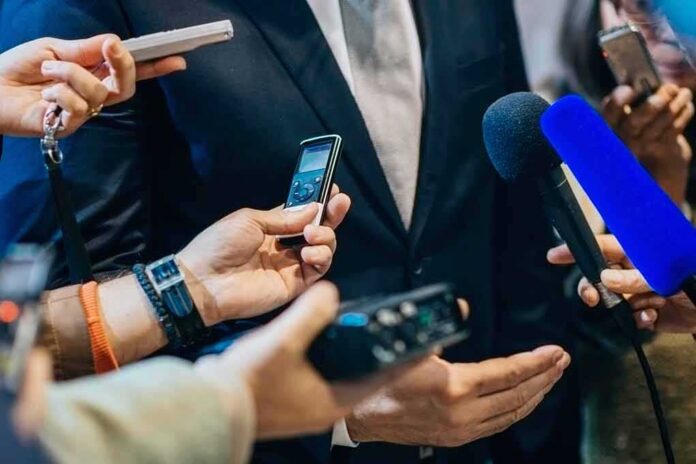 businessperson in suit surrounded by microphones and recorders