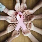 Hands forming a circle around a pink ribbon on a wooden table