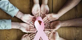 Hands forming a circle around a pink ribbon on a wooden table