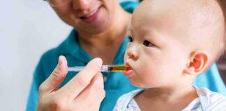 Baby taking liquid medicine from an oral syringe held by an adult