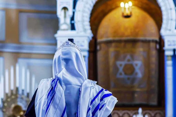 shutterstock_709900843-1 Person in white and blue prayer shawl facing ornate interior