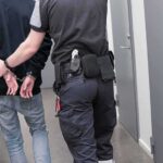 Japan Transfers Russian Mastermind to Germany Security officer escorts handcuffed person down hallway