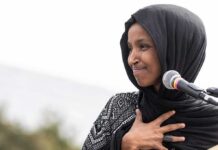 Feds SUBPOENA Ilhan Omar’s Family! Ilhan Omar speaking at a microphone with hand on chest