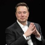 Elon Musk seated in a black suit with hands clasped