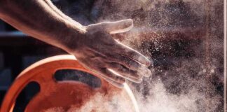 Athlete’s chalked hands above an orange weight plate